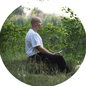 Ein Mann sitzt auf einer Wiese und meditiert.