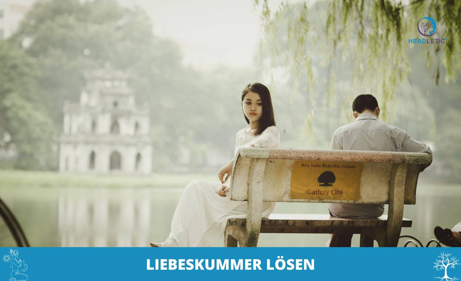 Eine Frau und ein Mann sitzen auf einer Bank neben einem See, mit dem Rücken zueinander. Der Mann blickt auf etwas in seinen Händen. Im Hintergrund sind eine Pagode und Bäume zu sehen. Der Text lautet „LIEBESKUMMER LÖSEN“.