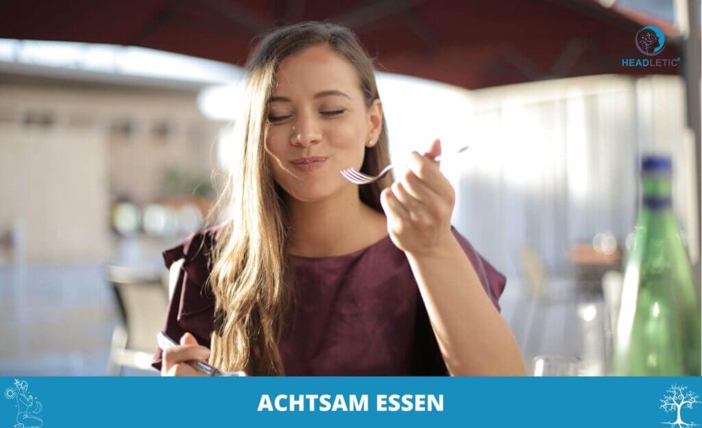 Frau mit langen Haaren sitzt an einem Tisch im Freien, genießt ihre Mahlzeit mit einer Gabel und sieht zufrieden aus. Der Text am unteren Rand lautet "Achtsames Essen.