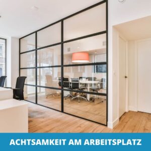 Modernes Büro mit Schreibtischen und Stühlen im Vordergrund, einem gläsernen Besprechungsraum mit rundem Tisch und Stühlen sowie einem Schild, das auf die Bedeutung von Achtsamkeit am Arbeitsplatz hinweist.