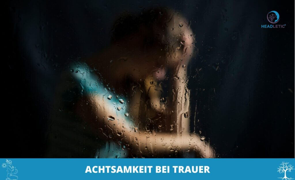 Eine Person sitzt hinter einem regenverhangenen Fenster, den Kopf auf die Hand gestützt. Der Text darunter, "Achtsamkeit bei Trauer", spiegelt das Thema der Achtsamkeit in der Trauer und der sanften Selbstwahrnehmung in schwierigen Zeiten wider.