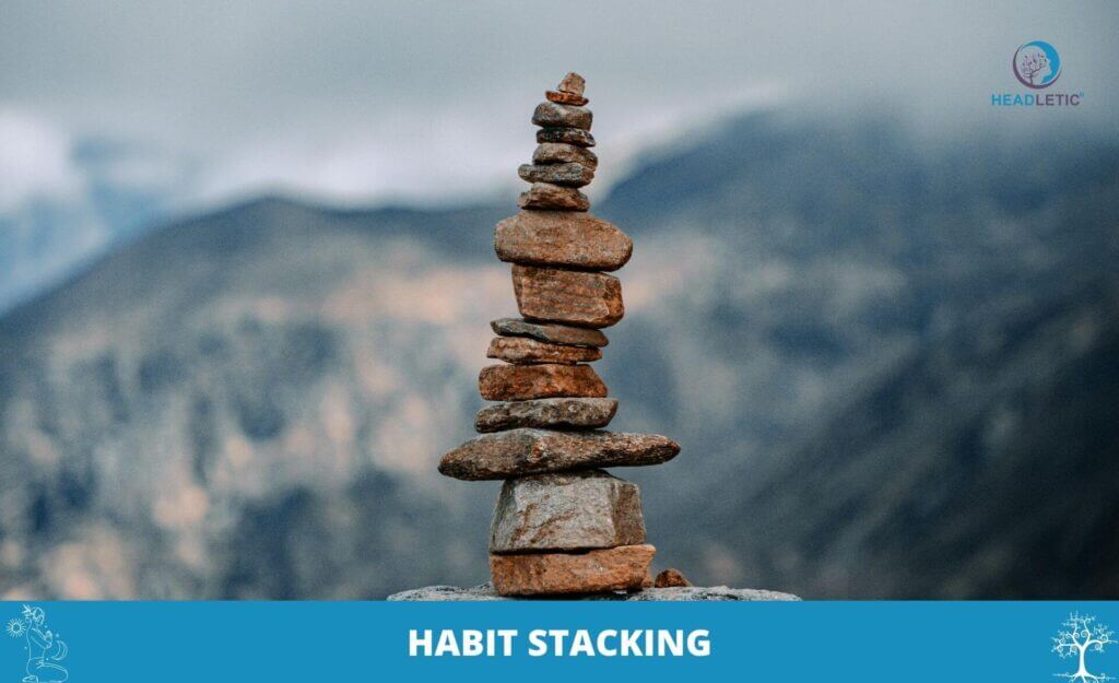 Ein hoher Stapel ungleichmäßiger Felsen, der im Freien balanciert wird, mit Bergen im Hintergrund, symbolisiert Habit Stacking, was durch die Worte "HABIT STACKING" am unteren Rand hervorgehoben wird.
