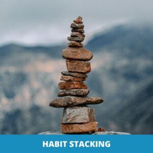 Ein hoher Stapel ungleichmäßiger Felsen, der im Freien balanciert wird, mit Bergen im Hintergrund, symbolisiert Habit Stacking, was durch die Worte "HABIT STACKING" am unteren Rand hervorgehoben wird.