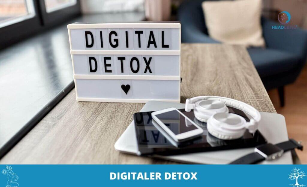 Ein Leuchtkasten mit der Aufschrift DIGITAL DETOX" steht auf einem Tisch neben Kopfhörern, einem Smartphone und einem Tablett - eine einladende Szene, die Sie zu Ihrem eigenen Digitaler Detox inspirieren soll.