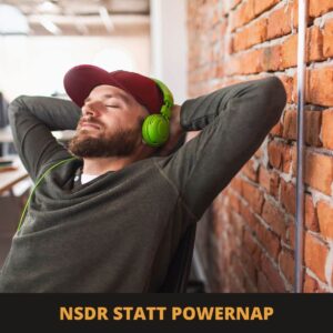 Ein Mann mit grünen Kopfhörern entspannt sich mit geschlossenen Augen an seinem Schreibtisch und lehnt sich in einem modernen Büro an eine unverputzte Backsteinwand. Der Text darunter lautet: „NSDR statt Powernap“ und unterstreicht damit seine Entscheidung, NSDR zu praktizieren, anstatt ein herkömmliches Powernap zu machen.