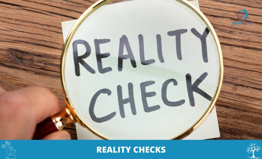 Eine Lupe zoomt auf einen Haftzettel mit der fettgedruckten Aufschrift „Reality Checks“, der auf einer Holzoberfläche liegt.